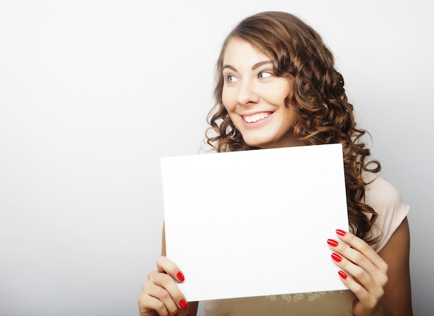 고립 된 회색 배경 위에 빈 간판을 보여주는 웃는 젊은 캐주얼 스타일의 여성