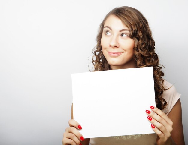 Sorridente giovane donna in stile casual che mostra cartello in bianco su sfondo grigio isolato