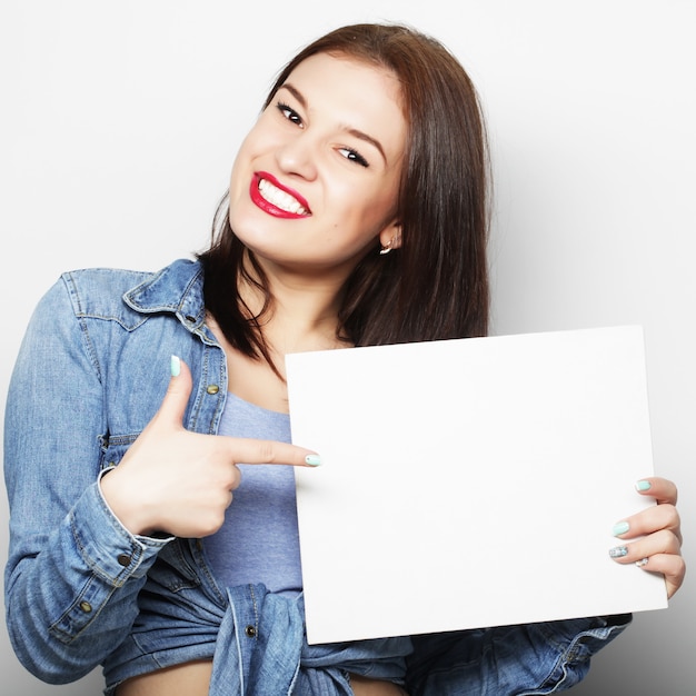 Sorridente giovane donna stile casual che mostra cartello bianco, su uno spazio bianco isolato