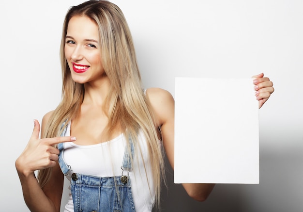 Foto sorridente giovane donna stile casual che mostra cartello bianco, su uno spazio bianco isolato