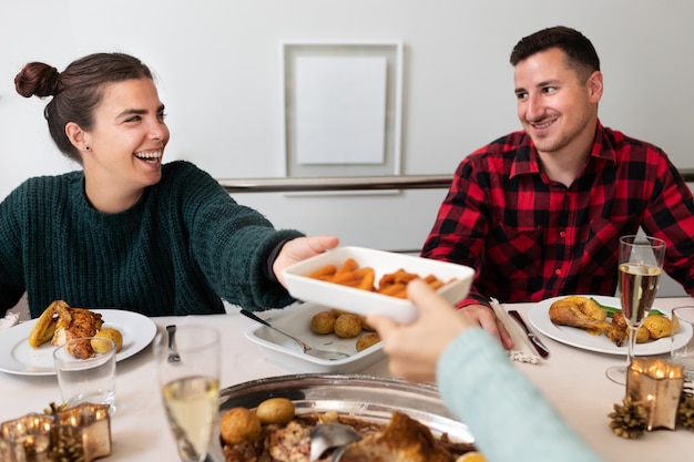 クリスマスの家族の夕食で若い白人カップルの笑顔いくつかの前菜を渡す休日