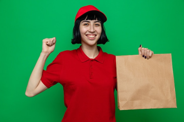 Foto sorridente giovane ragazza delle consegne caucasica che tiene in mano l'imballaggio degli alimenti e tiene il pugno