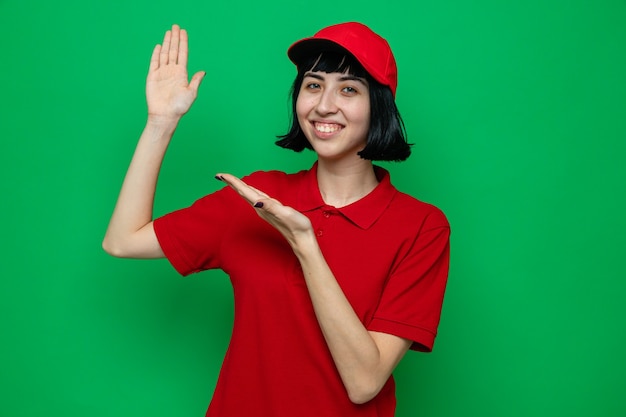 Smiling young caucasian delivery girl pointing at her hand 