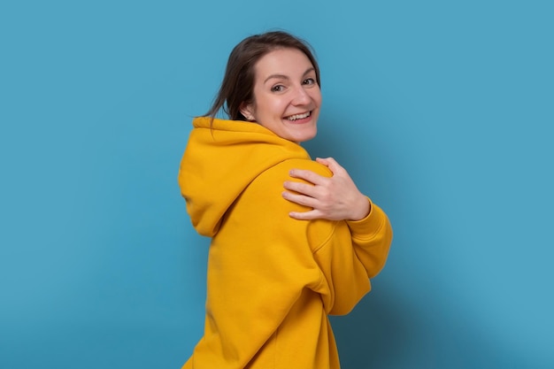Photo smiling young caucasian woman hugging herself feeling comfortable and cozy studio shot on blue wall