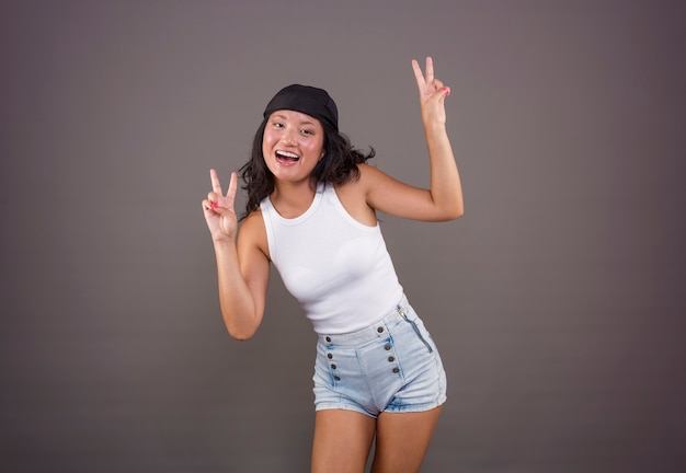 Smiling young chinese girl with bandana and shorts, making the peace or victory sign, in a funny pose and expression.