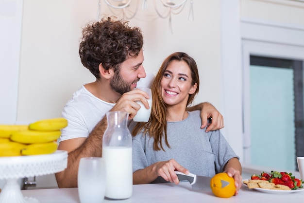 Smiling young couple cooking food in the kitchen together in the kitchen,having a great time together. Man and woman laughing and drinking milk in the morning with breakfast