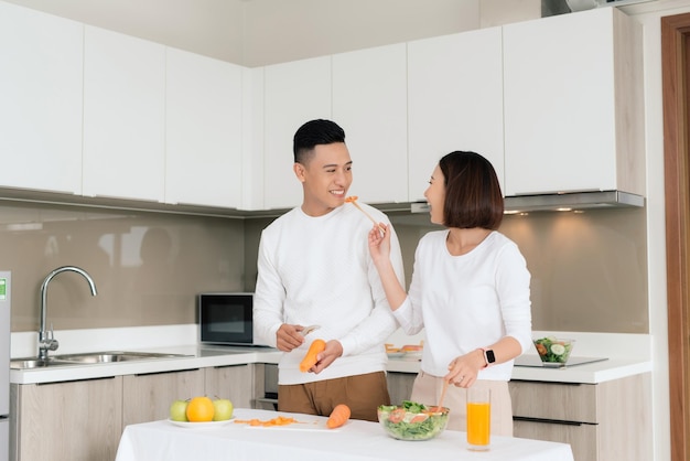 Giovani coppie sorridenti che cucinano alimento nella cucina