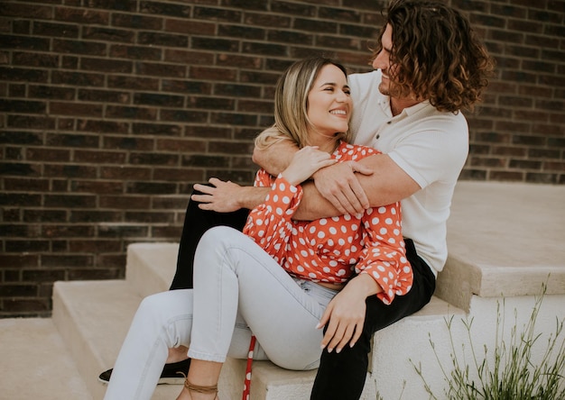 Foto giovani coppie sorridenti nell'amore che si siedono davanti al muro di mattoni della casa