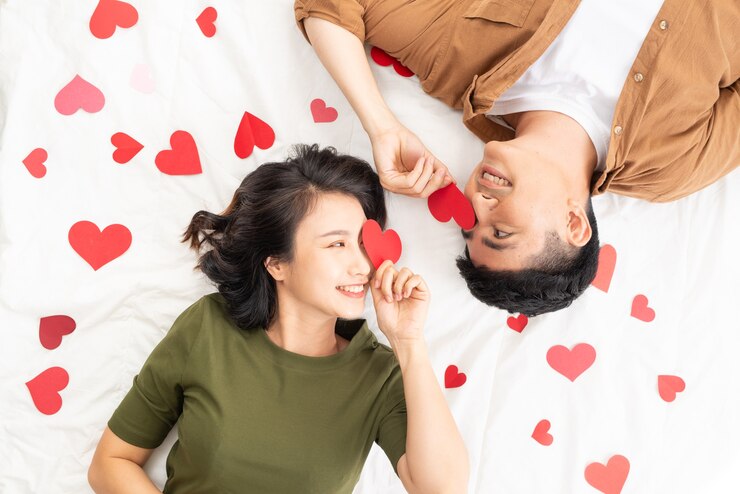 Photo 多くのハートの形でベッドに横たわって笑顔の若いカップル。