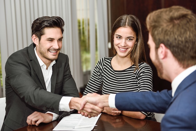 Smiling young couple shaking hands with an insurance agent