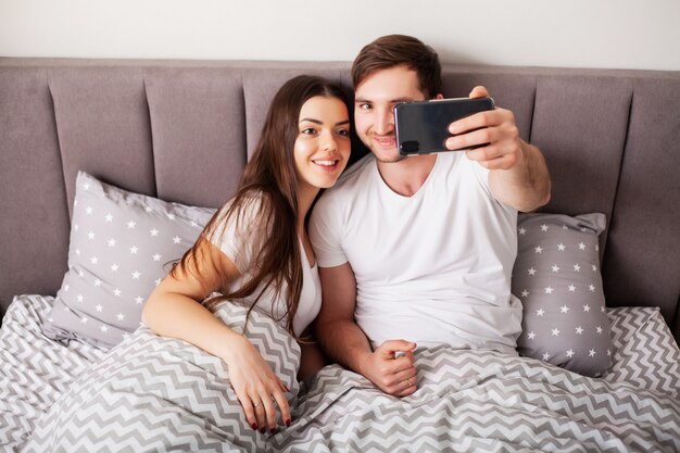 Giovani coppie sorridenti che prendono insieme selfie nella camera da letto