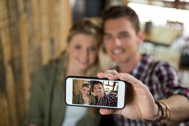 Smiling young couple taking selfie with cellphone in cafeteria