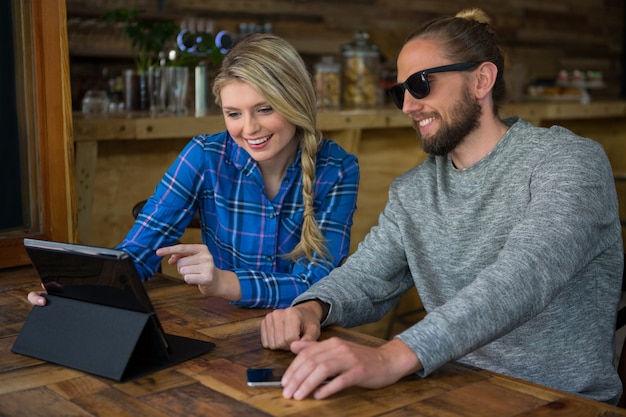 Smiling young couple using tablet PC at table in cafe