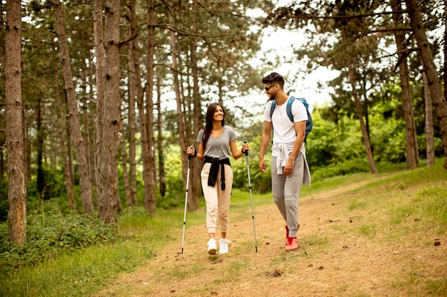 Smiling young couple walking with backpacks in the forest on a summer day