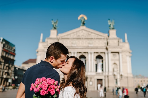 恋に花の花束と笑顔の若いカップルは、屋外で恋に抱き合っています。愛と優しさ、交際、ロマンス。ライフスタイルのコンセプト。