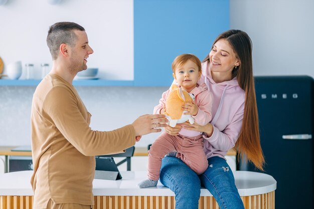 Smiling young couple with their adorable baby daughter playing together in living room at home