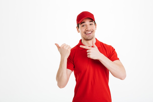 Smiling young delivery man pointing isolated