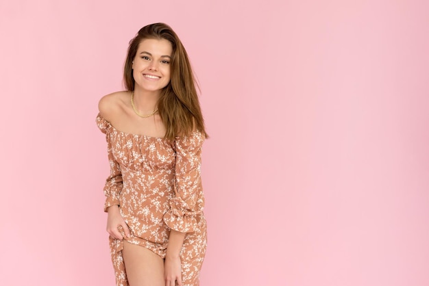 Smiling young enjoying caucasian woman in a summer dress on a pink background Charming lady in a beige outfit posing with a happy expression