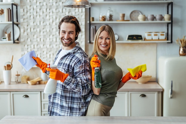 Photo smiling young european lady and guy in rubber gloves stand back to back with cleaning supplies in