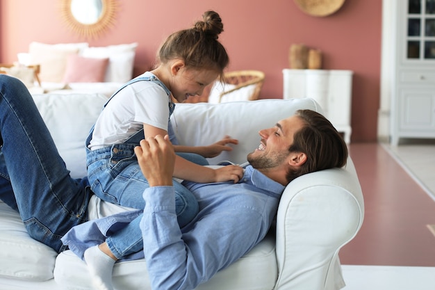 Улыбающийся молодой отец, лежа на диване в гостиной и играть со счастливой маленькой дочерью.