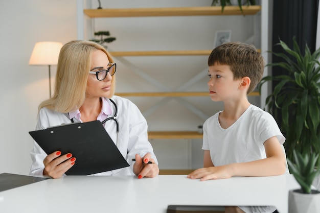 Smiling young female doctor or pediatrician talk comfort small\
boy patient at consultation in private clinic caring woman gp\
support cheer little kid examine consult in hospital healthcare\
concept