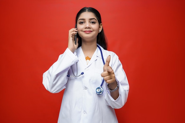 smiling young female doctor talking cell phone pointing finger front indian pakistani model