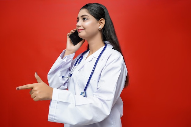 Photo smiling young female doctor talking cell phone pointing finger left indian pakistani model