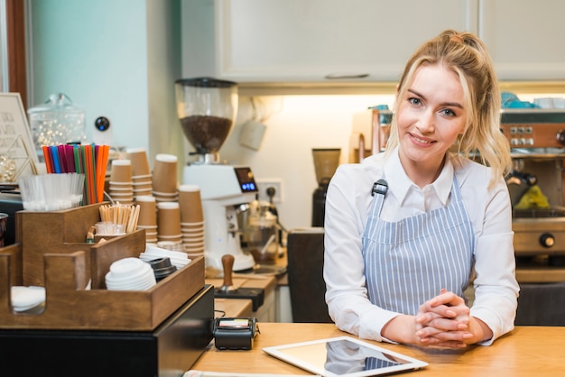 Foto giovane imprenditore femminile sorridente che sta nella caffetteria con la compressa digitale