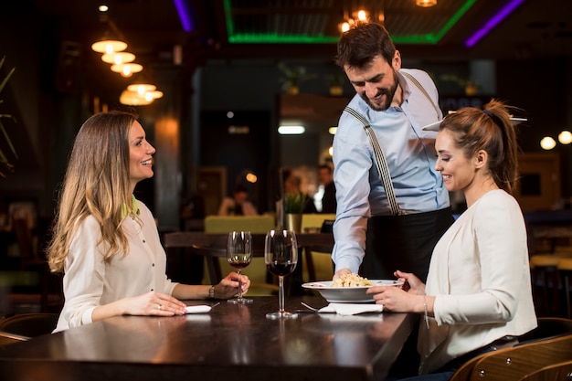 Smiling young female friends at a restaurant with waiter serving dinner