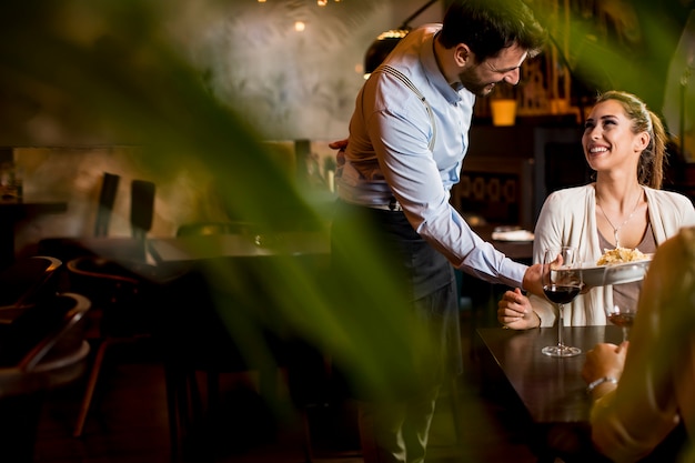 Smiling young female friends at a restaurant with waiter serving dinner