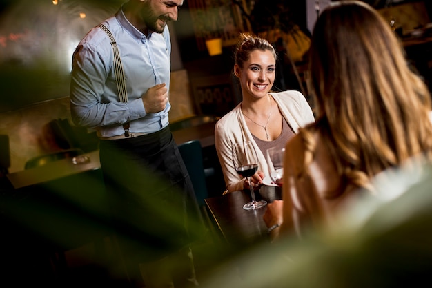 Smiling young female friends at a restaurant with waiter serving dinner