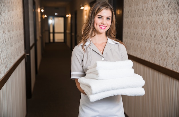 Foto giovane governante femminile sorridente che porta gli asciugamani piegati in corridoio dell'hotel