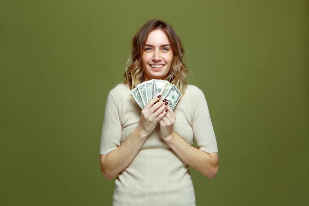 Smiling young female lottery winner showing bunch of dollar\
banknotes profit online casino win on