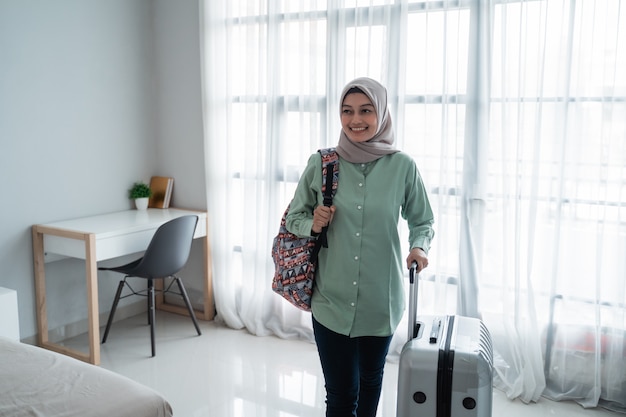 Smiling young female traveler carrying her bag and holding suitcase