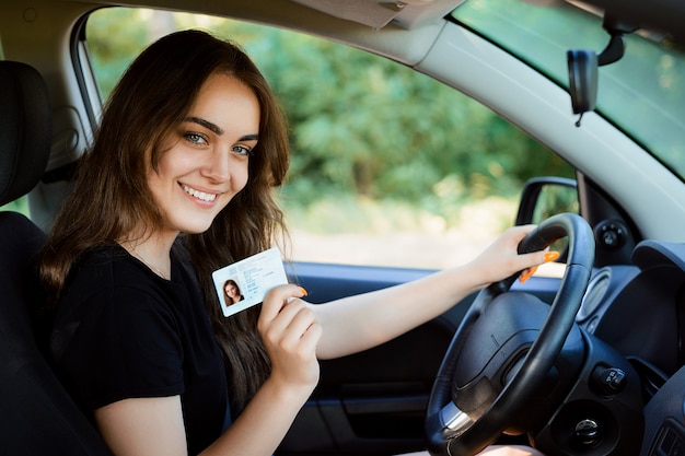 気持ちの良い外見で笑顔の若い女性は彼女の運転免許を誇らしげに示しています