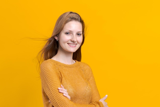 Smiling young female woman in yellow sweater posing isolated on pastel yellow