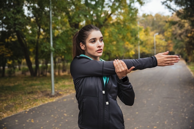 Smiling young fitness girl doing exercises at the park