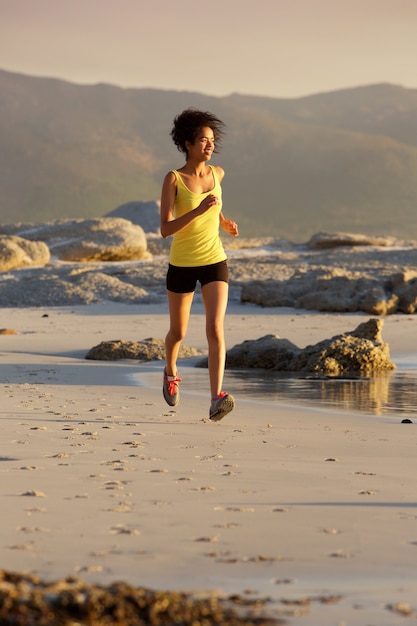 Smiling young fitness woman running on beach