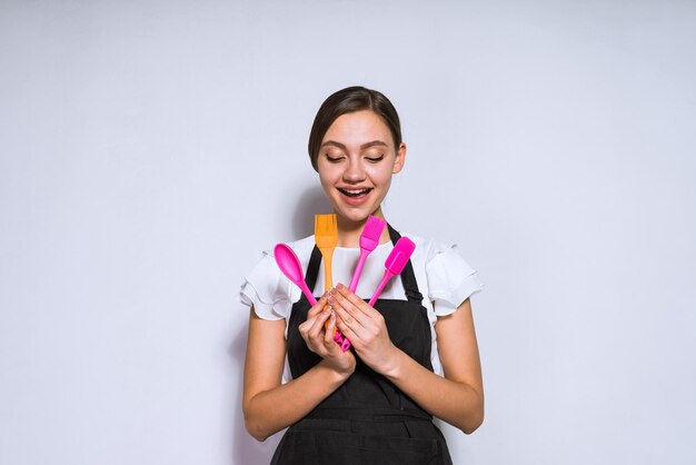 smiling young girl cook in black apron holding tools for baking and cooking