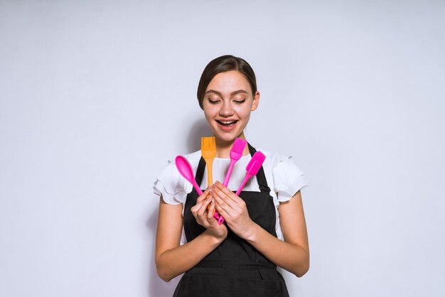 Smiling young girl cook in black apron holding tools for baking and cooking