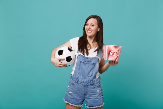 Photo smiling young girl football fan watching match support favorite team with soccer ball, bucket of popcorn isolated on blue turquoise background. people emotions, sport family leisure lifestyle concept.