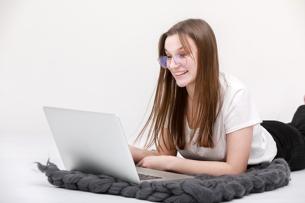 A smiling young girl in glasses sits with a laptop. Education, remote work and blogging. Isolated on a white background.