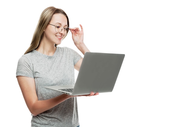 Photo a smiling young girl in glasses stands holding a laptop in her hands. freelance and education. isolated on a white wall. space for text.