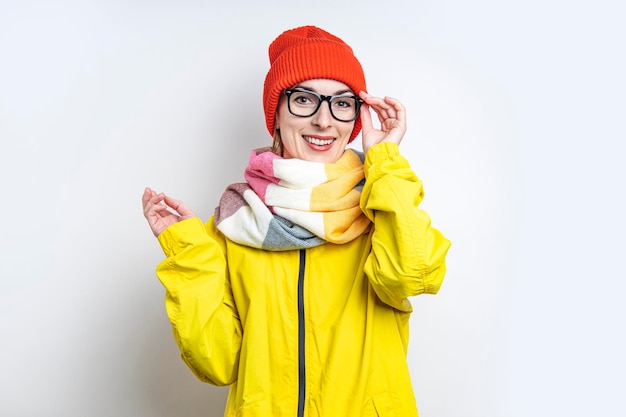 Smiling young girl in glasses in a yellow jacket on a light background