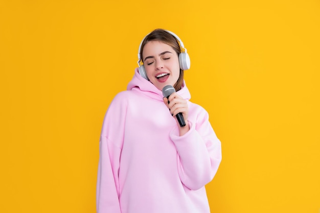 Smiling young girl in headphones with microphone on yellow background