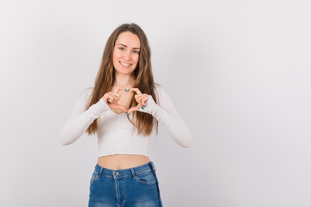 La ragazza sorridente sta mostrando il gesto del cuore su priorità bassa bianca