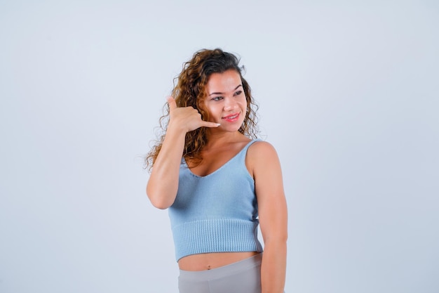 Smiling young girl is showing phone gesture with hand on white background