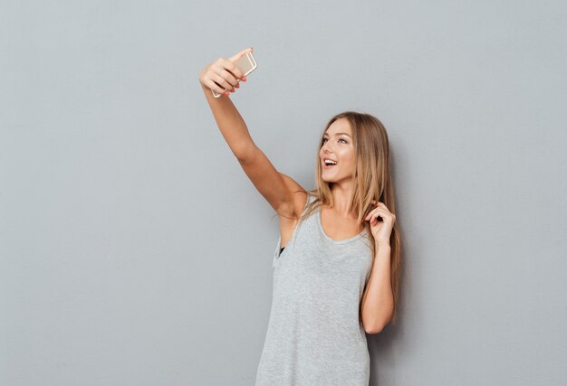 Smiling young girl making selfie photo on smartphone over gray background