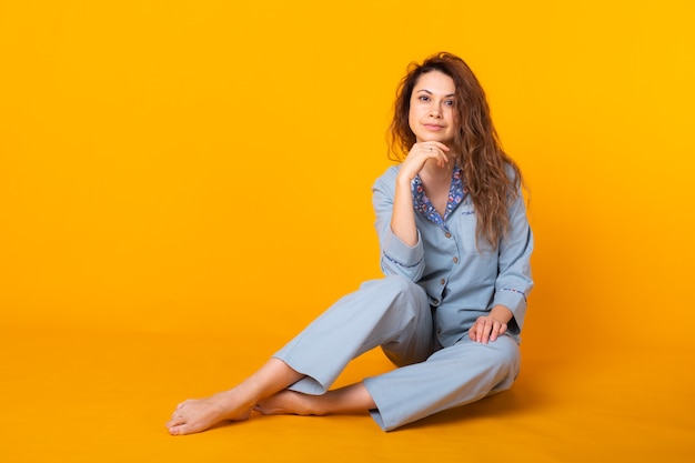 Smiling young girl in pajamas home wear posing while resting at home isolated on yellow wall