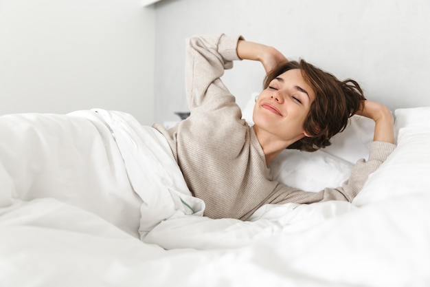 Smiling young girl relaxing in bed in the morning, stretching hands